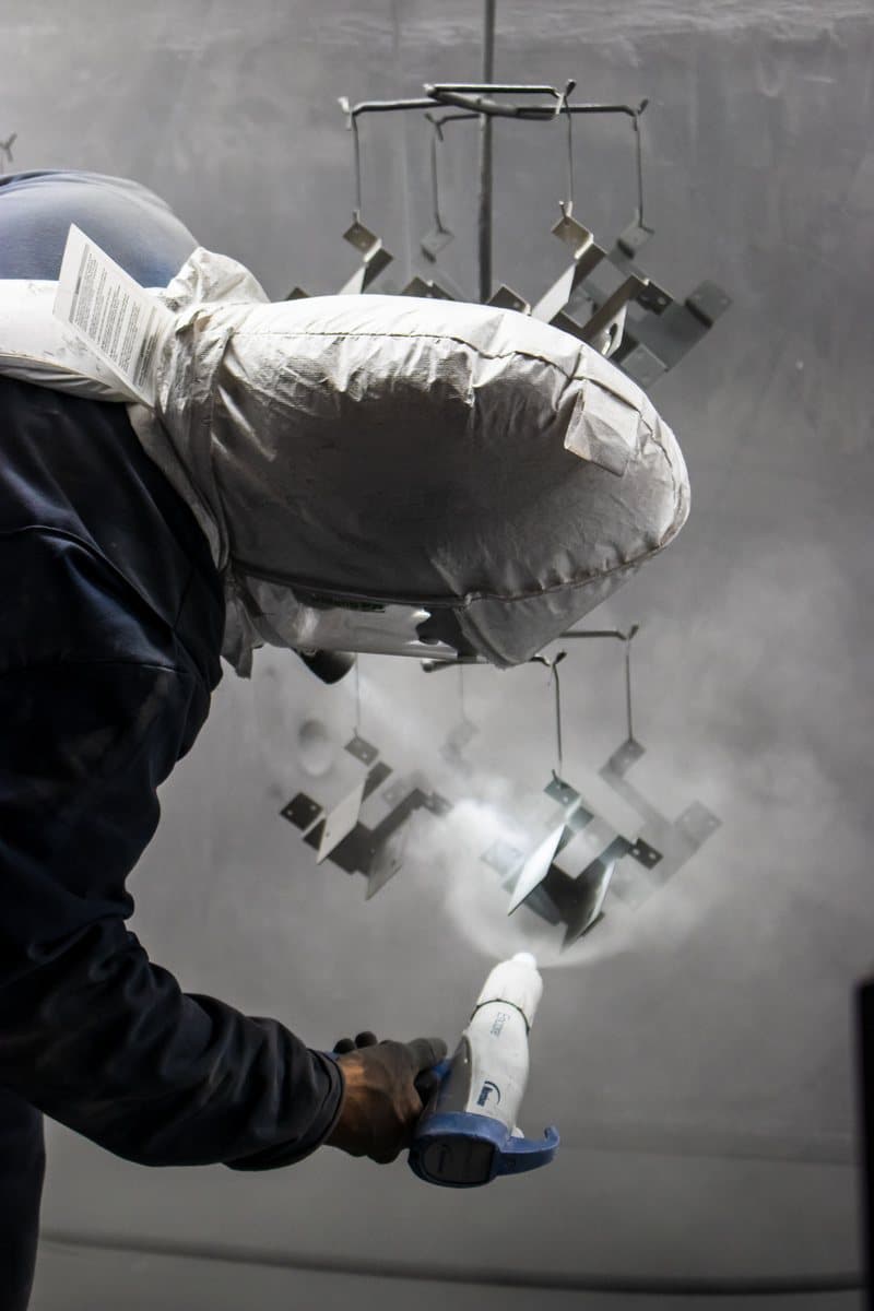 Technician applying powder coat to racked parts