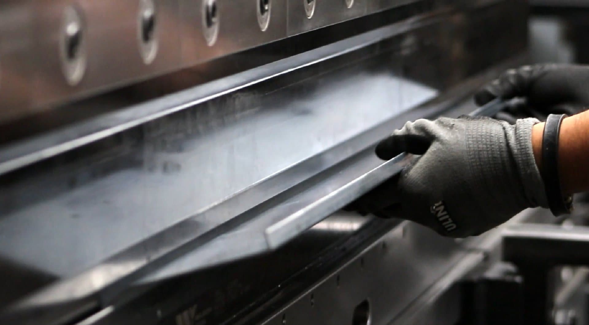 Gloved hand positioning a formed part in a press brake